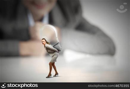 Carrying out an idea. Businesswoman looking at miniature of woman carrying bulb