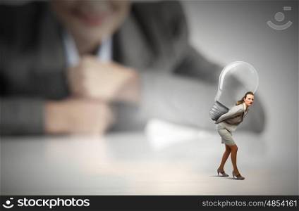 Carrying out an idea. Businesswoman looking at miniature of woman carrying bulb
