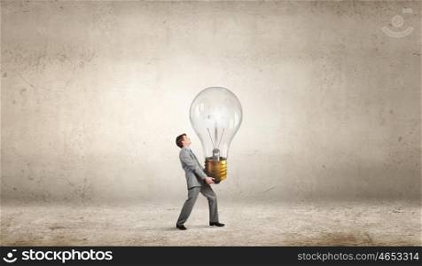Carrying out an idea. Young businessman carrying big light bulb in hands