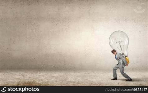 Carrying out an idea. Young businessman carrying big light bulb on back