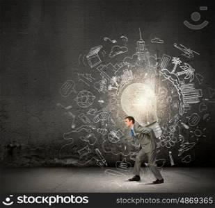 Carrying out an idea. Young businessman carrying big light bulb on back