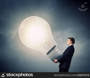Carrying out an idea. Young businessman carrying in hands big light bulb