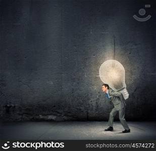 Carrying out an idea. Young businessman carrying light bulb on back