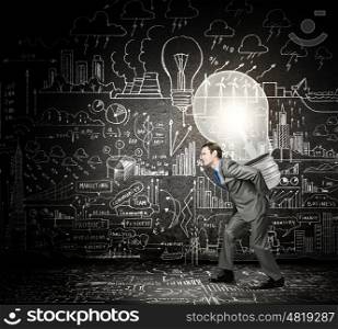 Carrying out an idea. Young businessman carrying light bulb on his back