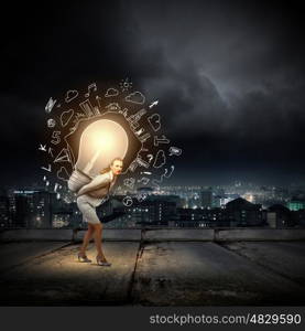 Carrying out an idea. Young businesswoman carrying big light bulb on back