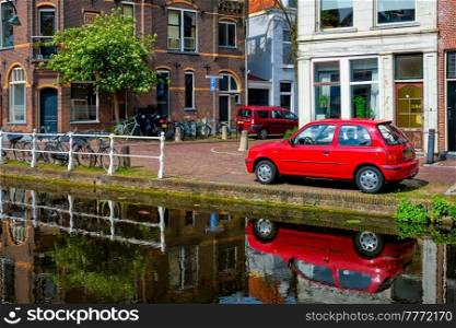 Cars and bicycles on canal embankment in street of Delft with reflection. Delft, Netherlands. Cars on canal embankment in street of Delft. Delft, Netherlands