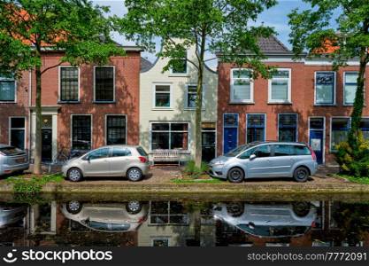 Cars and bicycles parked along the canal in street of Delft with reflection. Delft, Netherlands. Cars on canal embankment in street of Delft. Delft, Netherlands