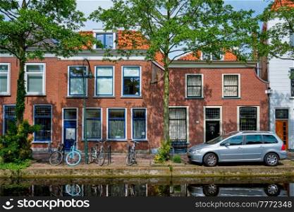 Cars and bicycles parked along the canal in street of Delft with reflection. Delft, Netherlands. Cars on canal embankment in street of Delft. Delft, Netherlands