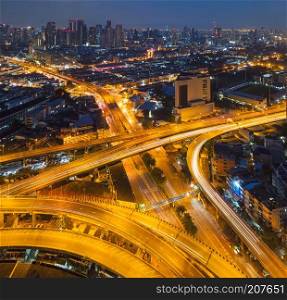 Cars driving on bridge roads shaped curve highways with skyscraper buildings. Aerial view of Expressway Bangna, Klong Toey in structure of architecture concept, Urban city, Bangkok at night, Thailand.