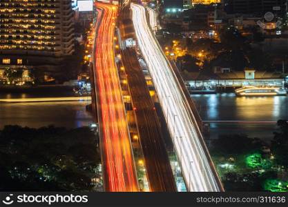 Cars light long exposure on Taksin Bridge in transportation concept. Train, boats lights with Chao Phraya River in Sathorn district, Bangkok City at night, Thailand