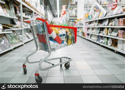 Cart full of goods in supermarket, nobody, shopping concept. Trolley with products in market, no people