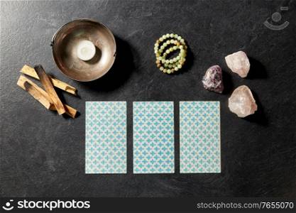 cartomancy, occult science and divination concept - tarot cards and different staff for magic ritual on slate stone background. tarot cards and magic staff for divination ritual