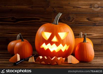 Carving of Halloween pumpkins in progress, pieces and cutting knife on wooden background, lantern is glowing. Carving of Halloween pumpkin