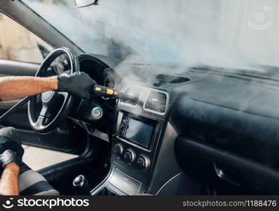Carwash service, male worker in gloves cleans salon with steam cleaner. Professional dry cleaning of car interior. Carwash, worker cleans salon with steam cleaner