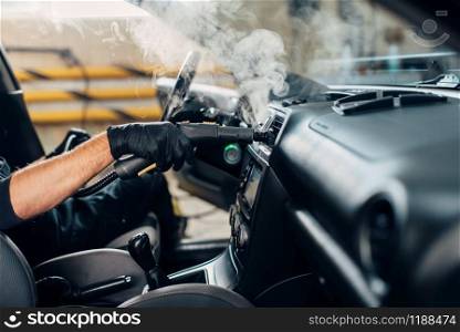 Carwash service, male worker in gloves removing dust and dirt with steam cleaner. Professional dry cleaning of car interior. Carwash, removing dust and dirt with steam cleaner
