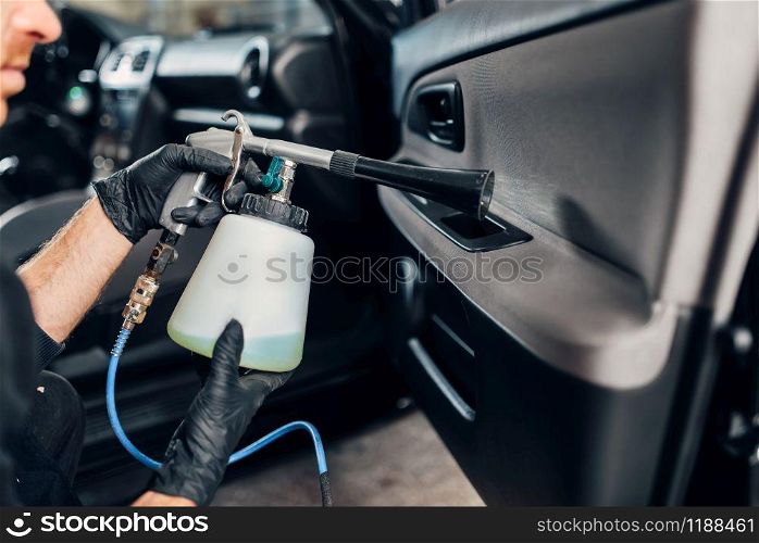 Carwash service, male worker in gloves using special spray. Professional dry cleaning of car door trim, vehicle interior hygiene