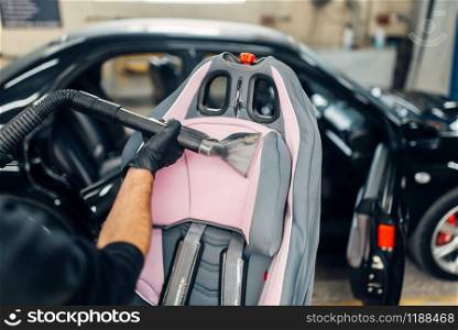 Carwash service, worker in gloves removing dust and dirt from child seat. Professional dry cleaning of car interior with vacuum cleaner. Carwash, removing of dust and dirt from child seat