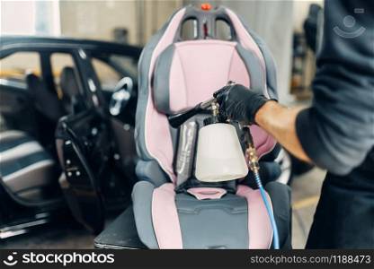 Carwash service, worker removing dust and dirt from child seat. Professional dry cleaning of car interior with vacuum cleaner. Carwash, removing of dust and dirt from child seat