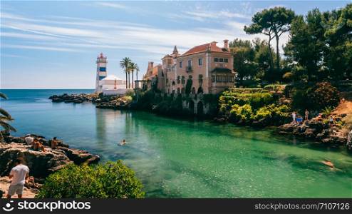 Cascais, Lisbon, Portugal - August 29, 2019: View of Santa Marta lighthouse and Municipal museum of Cascais, in Portugal with tourists bathing in the beautiful green water on a sunny summer day. View of Santa Marta lighthouse and Municipal museum of Cascais, in Portugal with tourists bathing