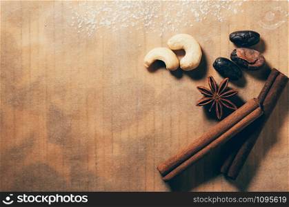 Cashew nuts, cinnamon sticks, cocoa beans and star anise on a table with empty space at one corner