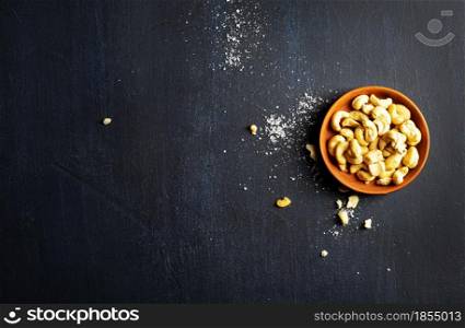 Cashew nutsin claim bowl, on dark background. Roasted cashew nuts
