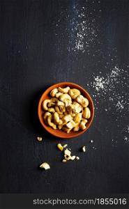 Cashew nutsin claim bowl, on dark background. Roasted cashew nuts
