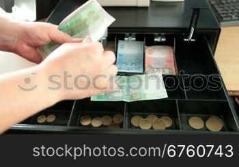 Cashier counting Ukrainian money hryvnya from the cash register drawer