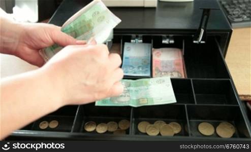 Cashier counting Ukrainian money hryvnya from the cash register drawer