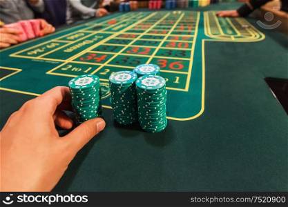 Casino, gambling and entertainment concept - male hand with stack of poker chips on a green table background. Casino, gambling and entertainment concept