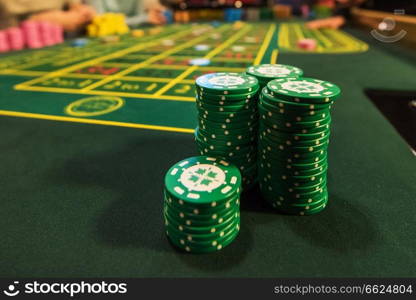 Casino, gambling and entertainment concept - stack of poker chips on a green table. Casino, gambling and entertainment concept