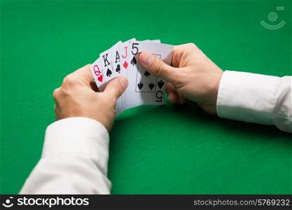 casino, gambling, poker, people and entertainment concept - close up of poker player holding playing cards at green casino table
