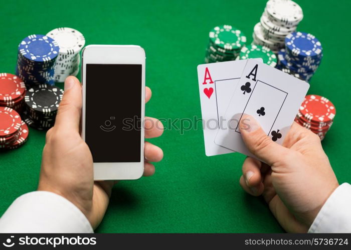 casino, online gambling, technology and people concept - close up of poker player with playing cards, smartphone and chips at green casino table