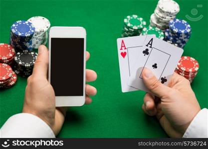 casino, online gambling, technology and people concept - close up of poker player with playing cards, smartphone and chips at green casino table