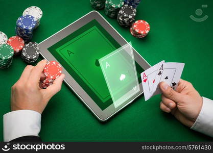 casino, online gambling, technology and people concept - close up of poker player with playing cards, tablet pc computer and chips at green casino table