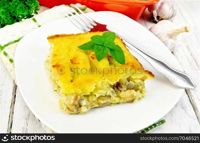 Casserole from mashed potatoes with a fish fillet in a plate on a towel against a light wooden board