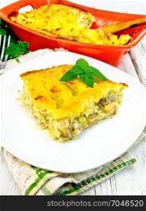 Casserole from mashed potatoes with fish fillets in a plate on a napkin on a wooden board background