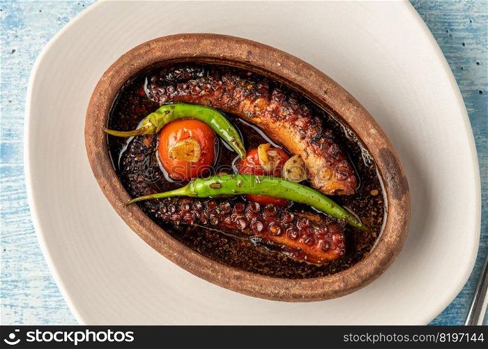 Casserole octopus with tomatoes and peppers on blue stone background