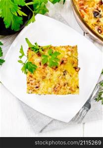 Casserole of minced meat, onion and eggplant doused with a sauce of eggs, milk, cheese and flour in a plate on towel on wooden board background from above