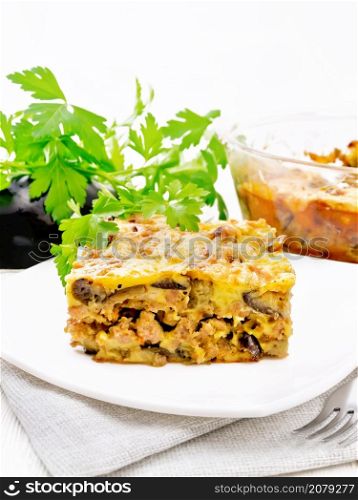 Casserole of minced meat, onions and eggplants doused with a sauce of eggs, milk, cheese and flour in a plate on napkin against the background of light wooden board