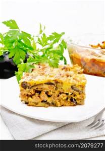 Casserole of minced meat, onions and eggplants doused with a sauce of eggs, milk, cheese and flour in a plate on napkin against the background of light wooden board