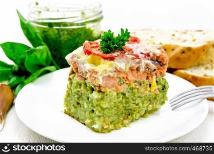 Casserole of salmon and rice with pesto, tomato and cheese in plate, bread, garlic and a jar of sauce on wooden board background