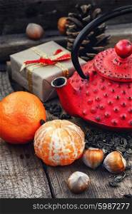 Cast iron kettle red,tangerine,tea leaves on wooden background
