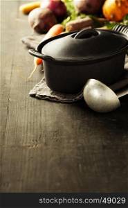 Cast iron pot and vegetables on wooden rustic table. Homemade food, cooking, vegetarian concept