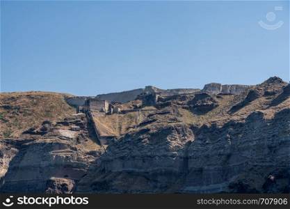 Castle and walls on cliffside and the mountaintop of Santorini. Castle walls of fortress on volcanic caldera island by Santorini