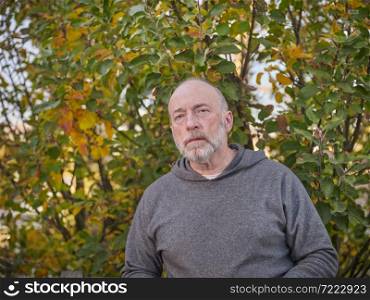 casual backyard portrait of a senior, confident, serious, bald man in sweatshirt with an apple tree in background