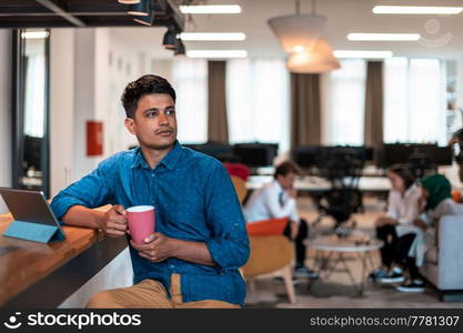Casual businessman taking a break from the work using a laptop while drinking tea in relaxation area of modern open plan startup office. High-quality photo. Casual business man taking break from the work using laptop while drinking tea in relaxation area of modern open plan startup office