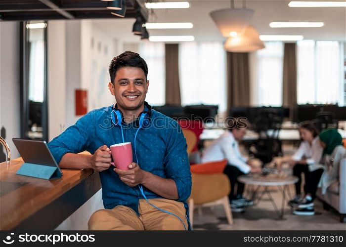 Casual businessman taking a break from the work using a laptop while drinking tea in relaxation area of modern open plan startup office. High-quality photo. Casual business man taking break from the work using laptop while drinking tea in relaxation area of modern open plan startup office