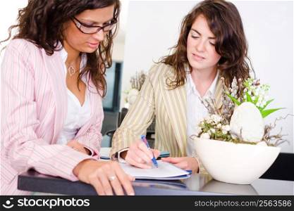 Casual businesswomen working together in team at office reception, looking at documents, talking.