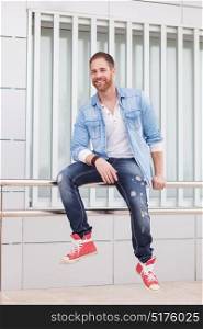 Casual guy with denim clothes sitting on a railing in the street