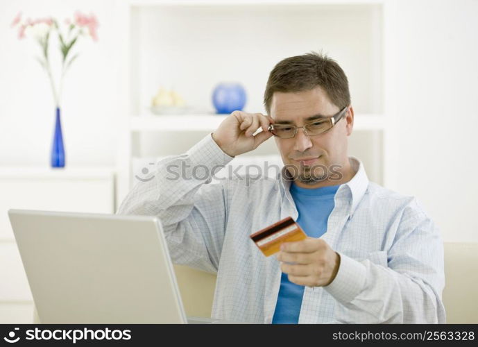 Casual man at home using laptop computer purchasing by credit card.